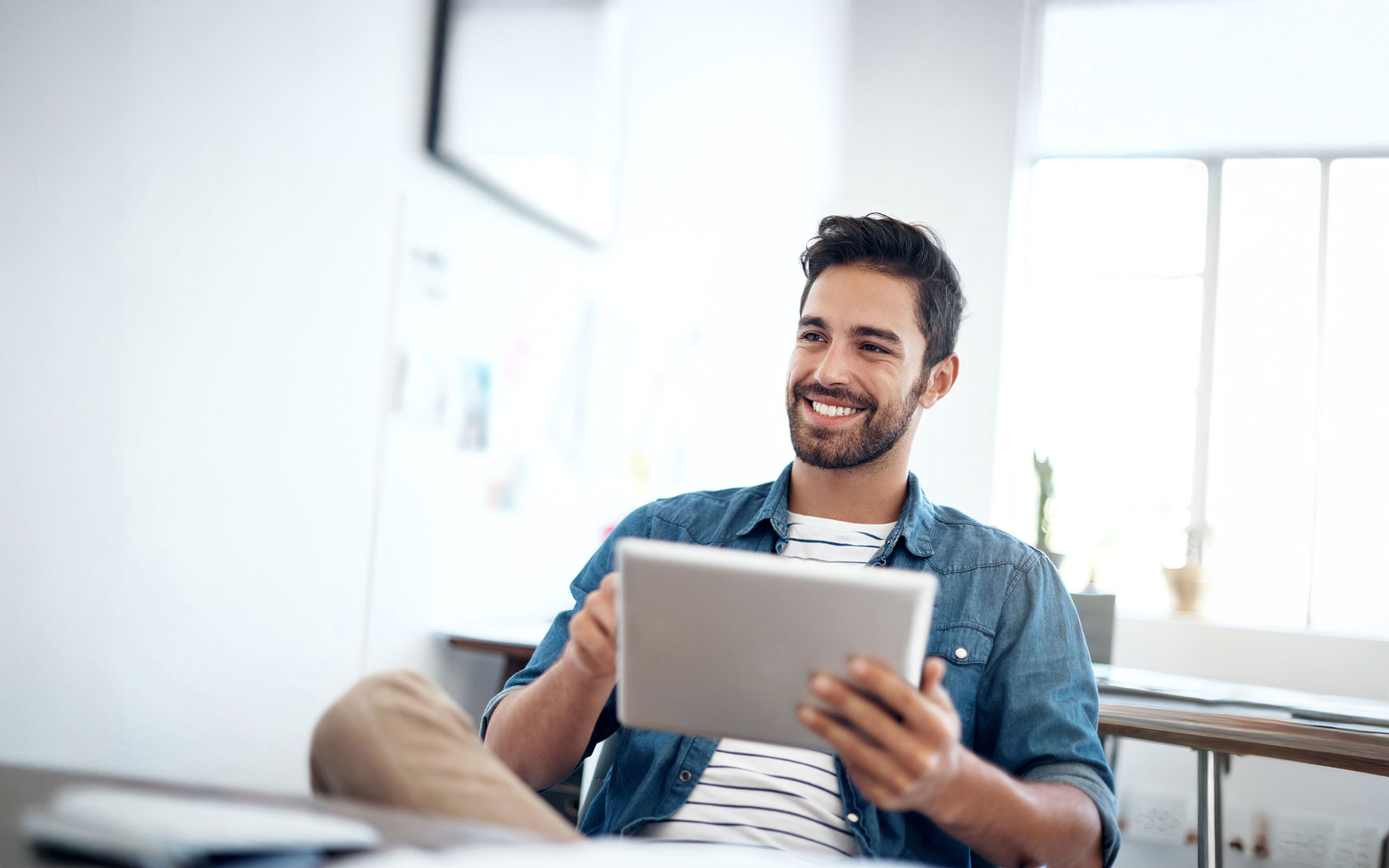 Dunkelhaariger Mann in Jeanshemd am Tablet